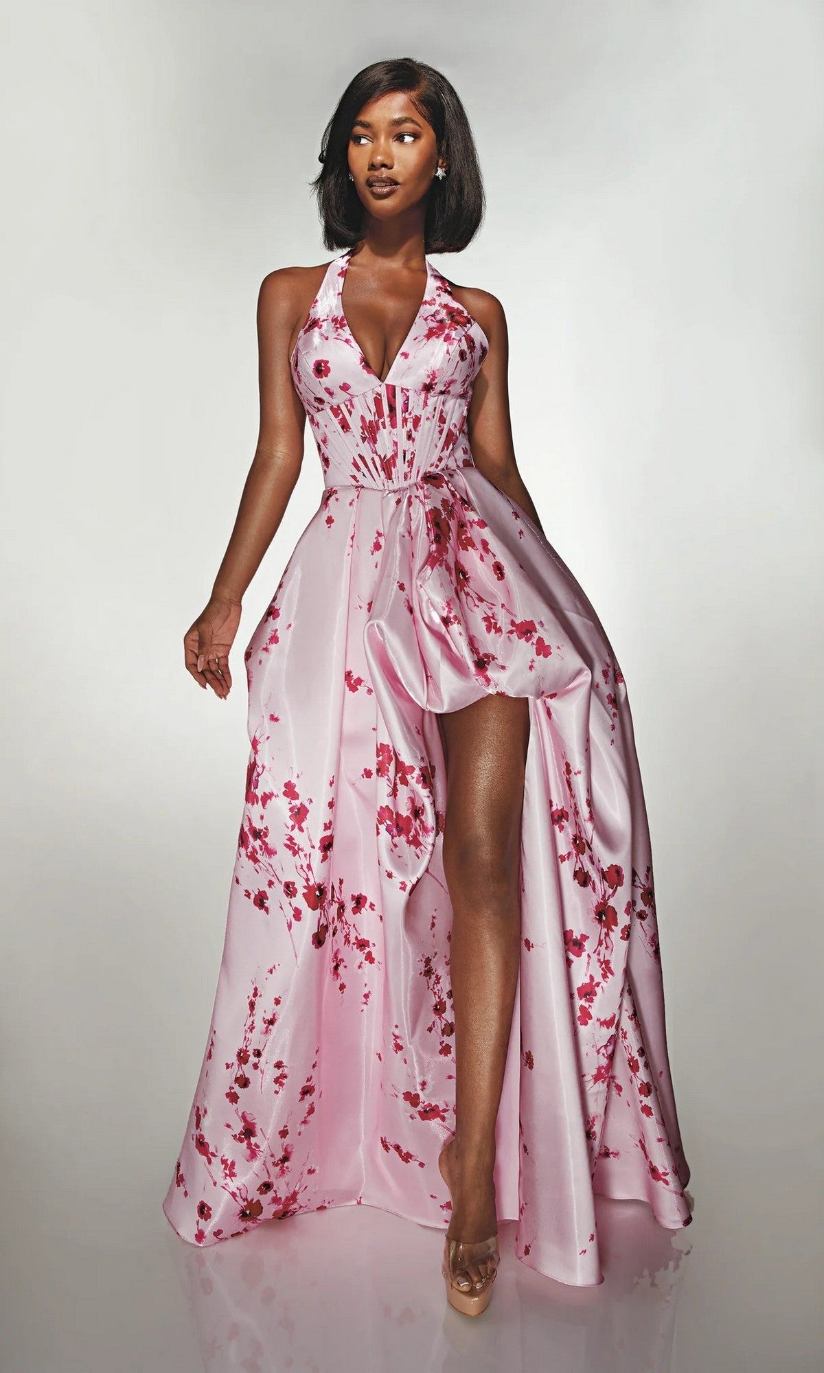 A woman models the Alyce 62214 long formal dress in cherry blossom, featuring a sleeveless floral satin design with a halter neckline and high slit, posed against a plain light background.